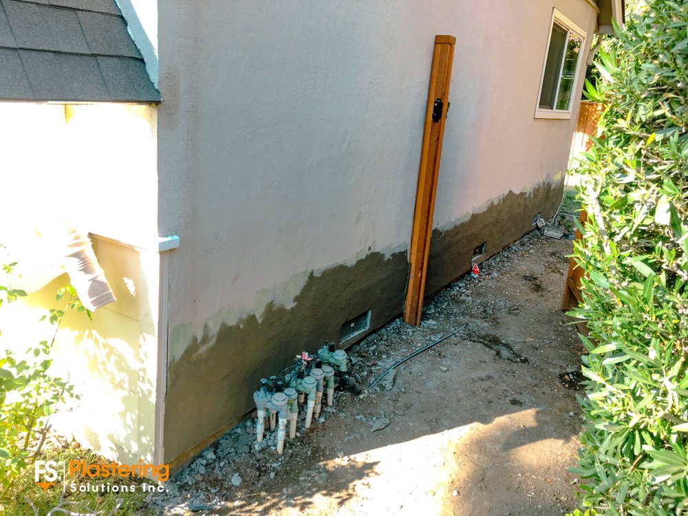 Base coat stucco applied along a side wall beside a fence post