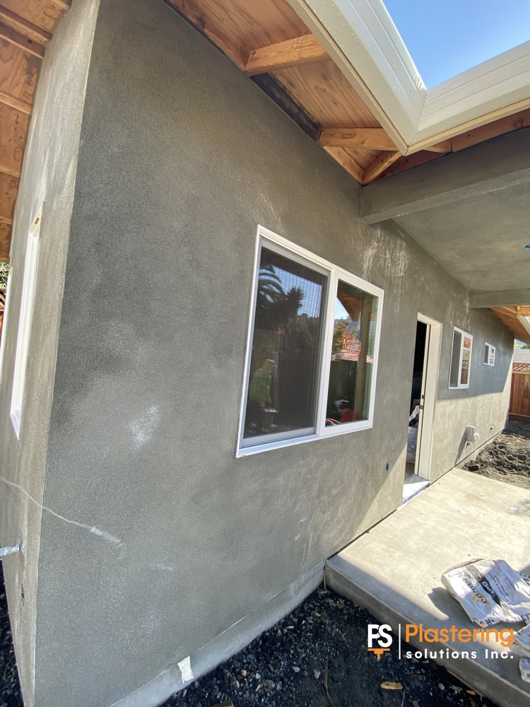 Finished stucco wall beside a new window and covered patio
