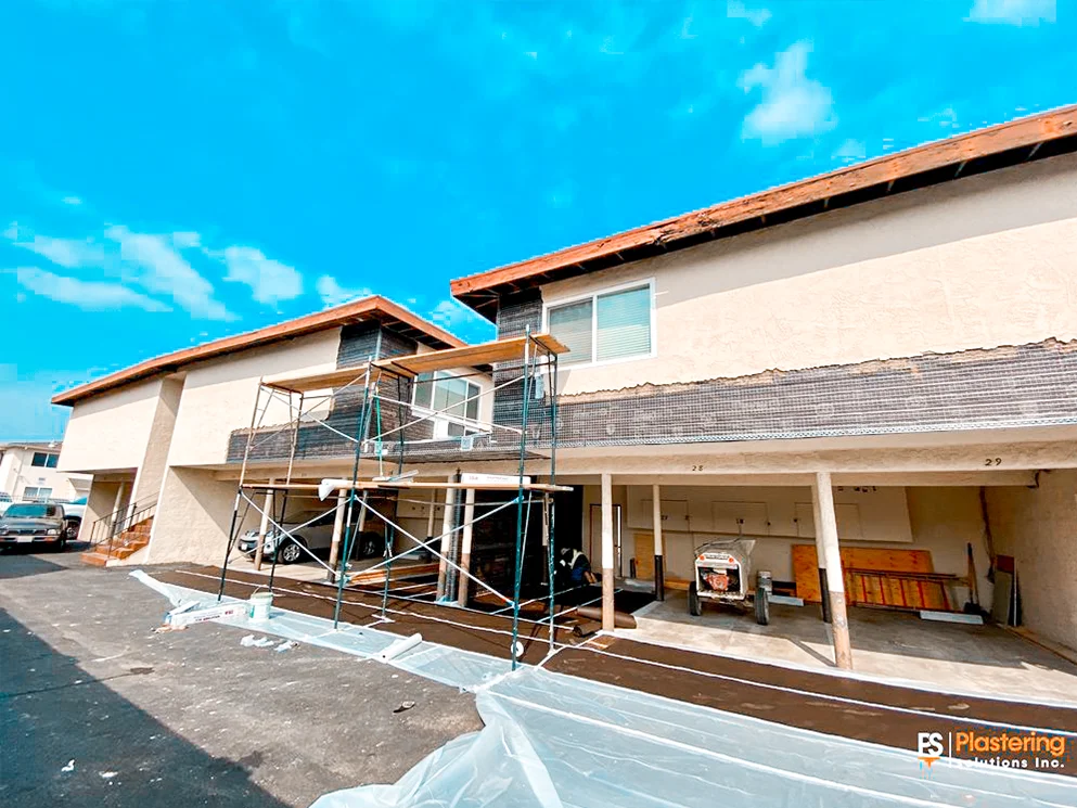 Apartment building elevation under active stucco renovation with scaffolding and protected walkways