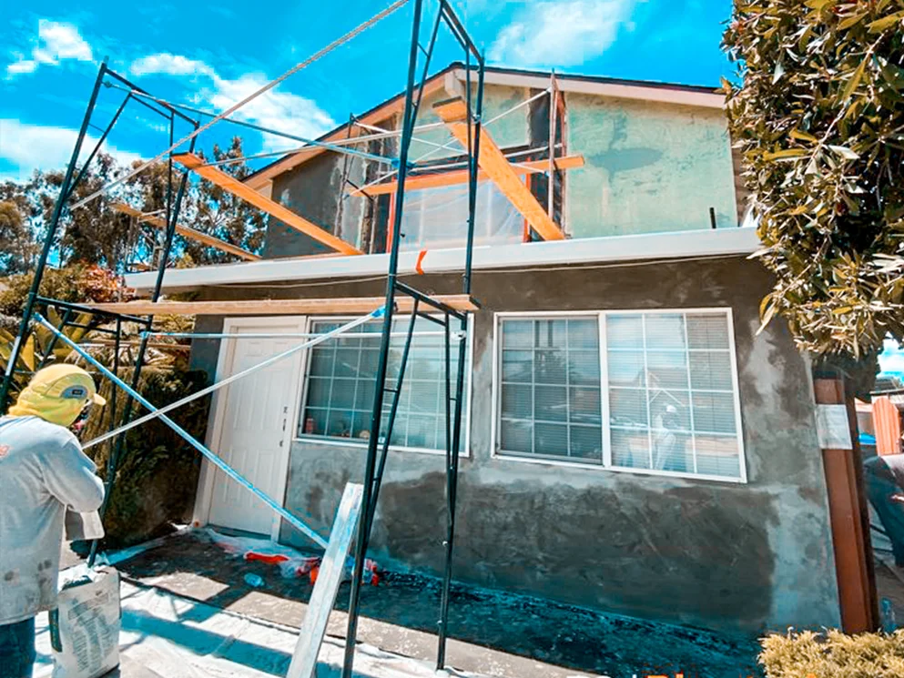 Crew member working beside the front elevation during the base coat stage