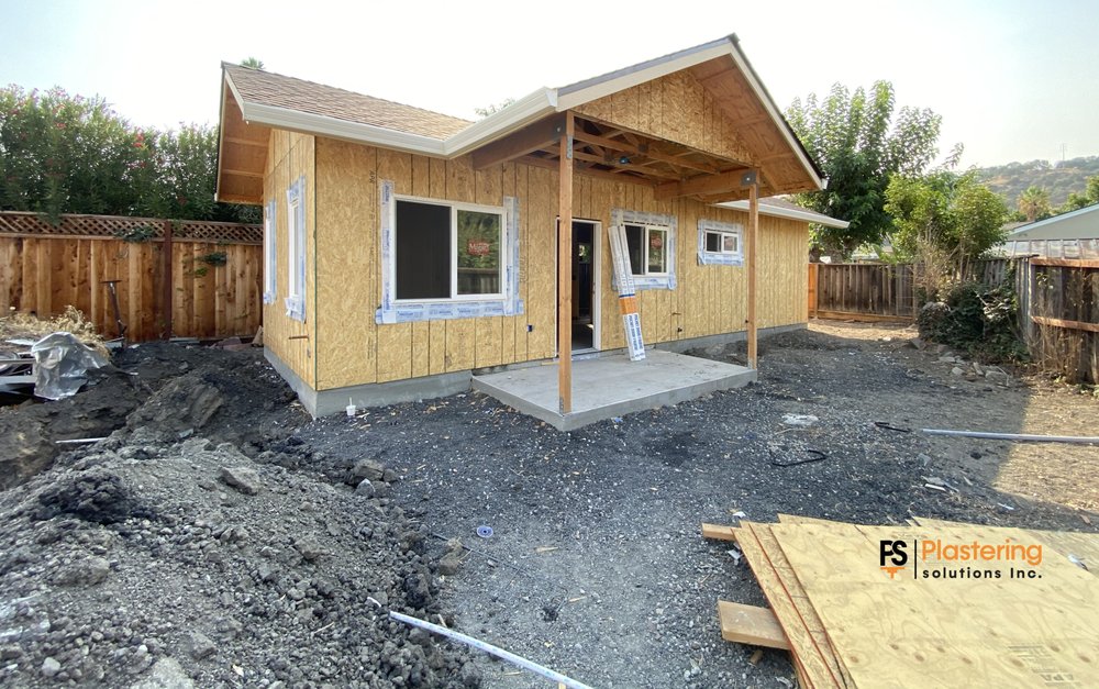 New house with plywood sheathing, taped windows, and a covered porch before stucco