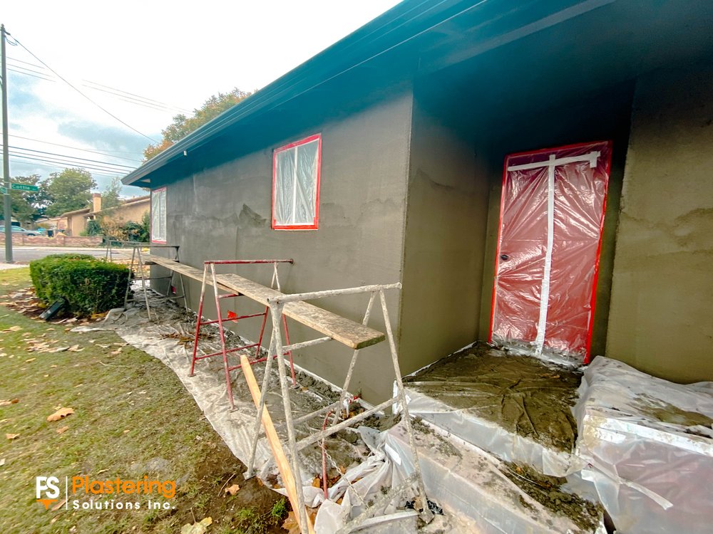 Scratch coat applied around a masked door with the ground covered in plastic