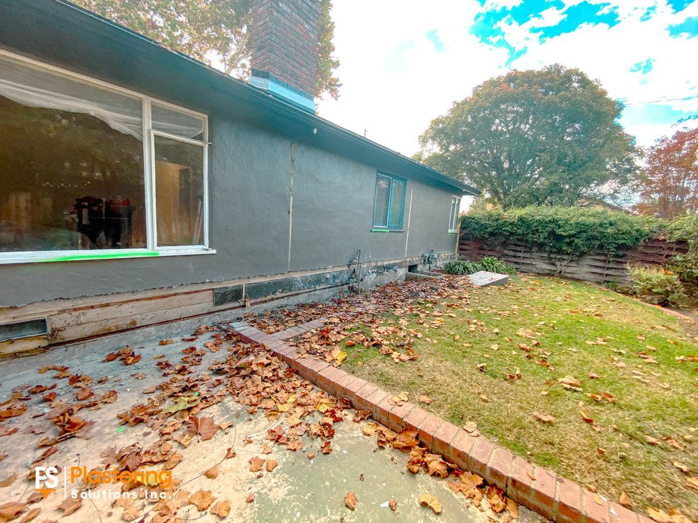 Side of the home with the lower stucco removed along the foundation beside the yard