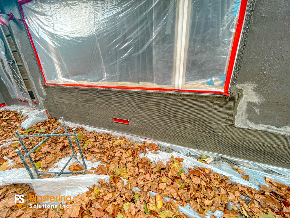 Scratch coat below a masked window with the ground protected by plastic