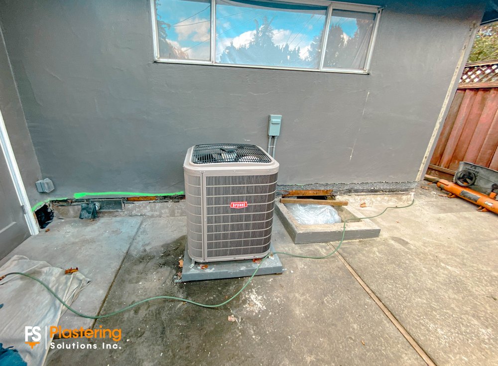 Rear wall with the stucco base removed along the foundation behind an air conditioning unit