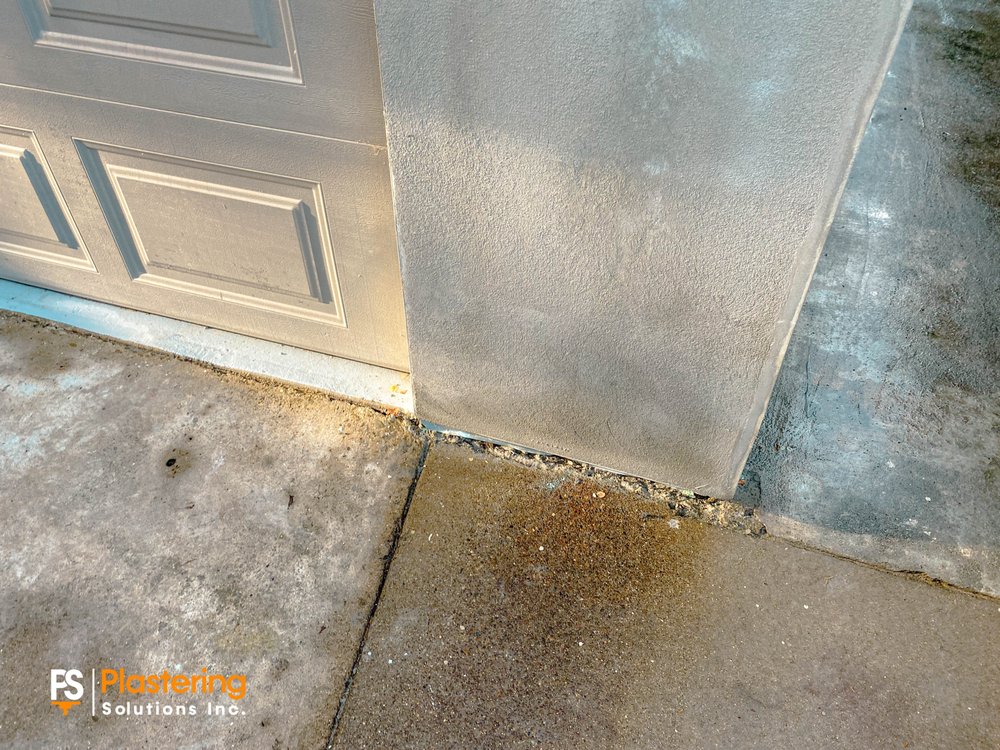 Finished stucco at the base of a garage corner beside the driveway