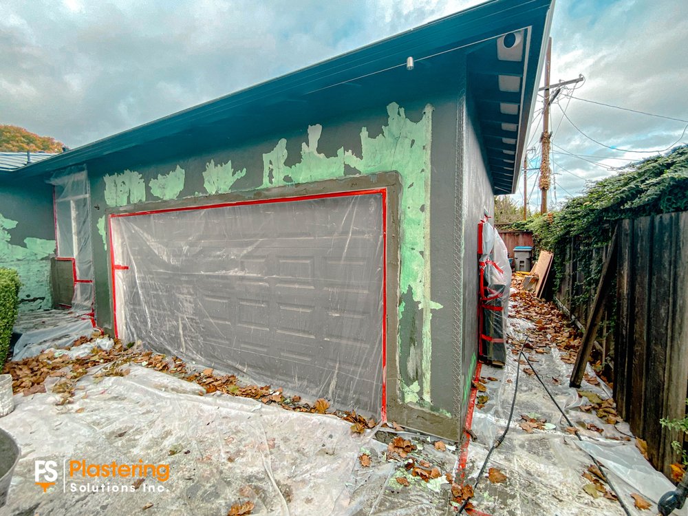 Garage wall with old paint layers exposed and the door masked for stucco