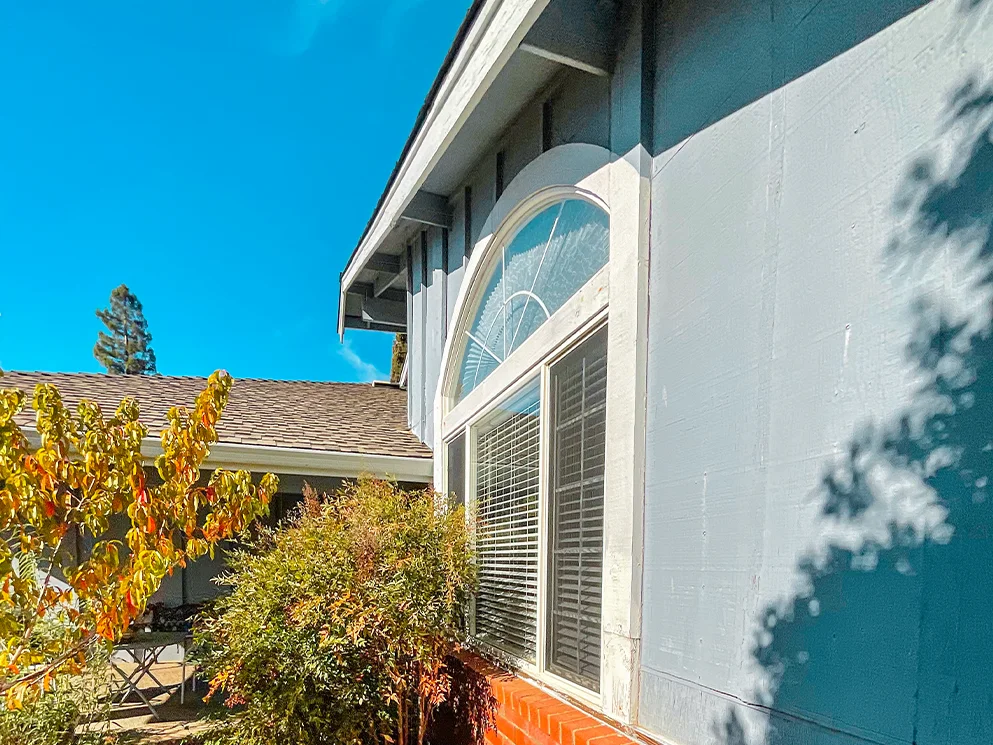 Side wall with painted board siding beside an arched window before conversion