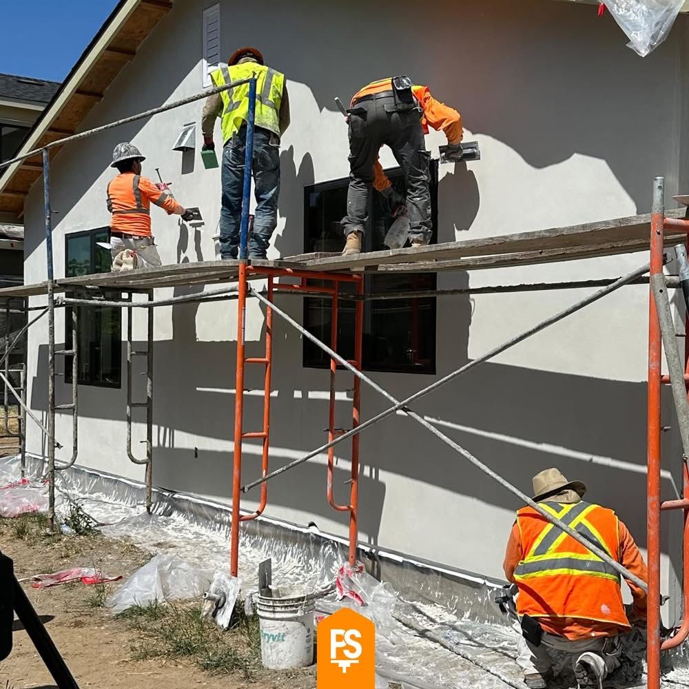 Four Plastering Solutions Inc crew members on scaffolding troweling and floating a gray finish coat across the stucco walls of a house on a sunny day
