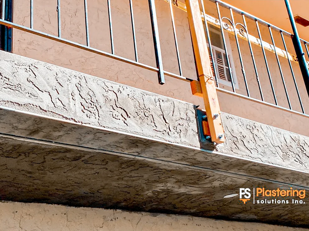Fresh stucco repair along an apartment balcony beam beneath a metal railing