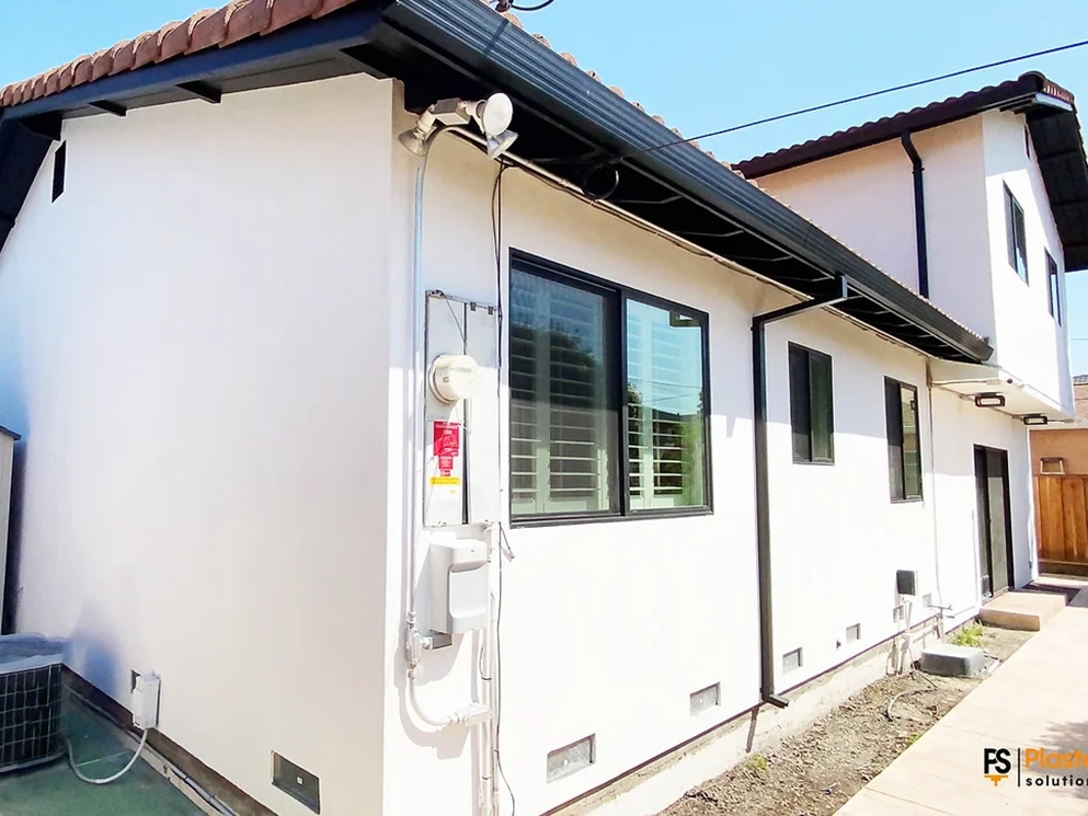 Side elevation of a San Jose home finished in smooth white stucco with black windows after a demo to paint remodel