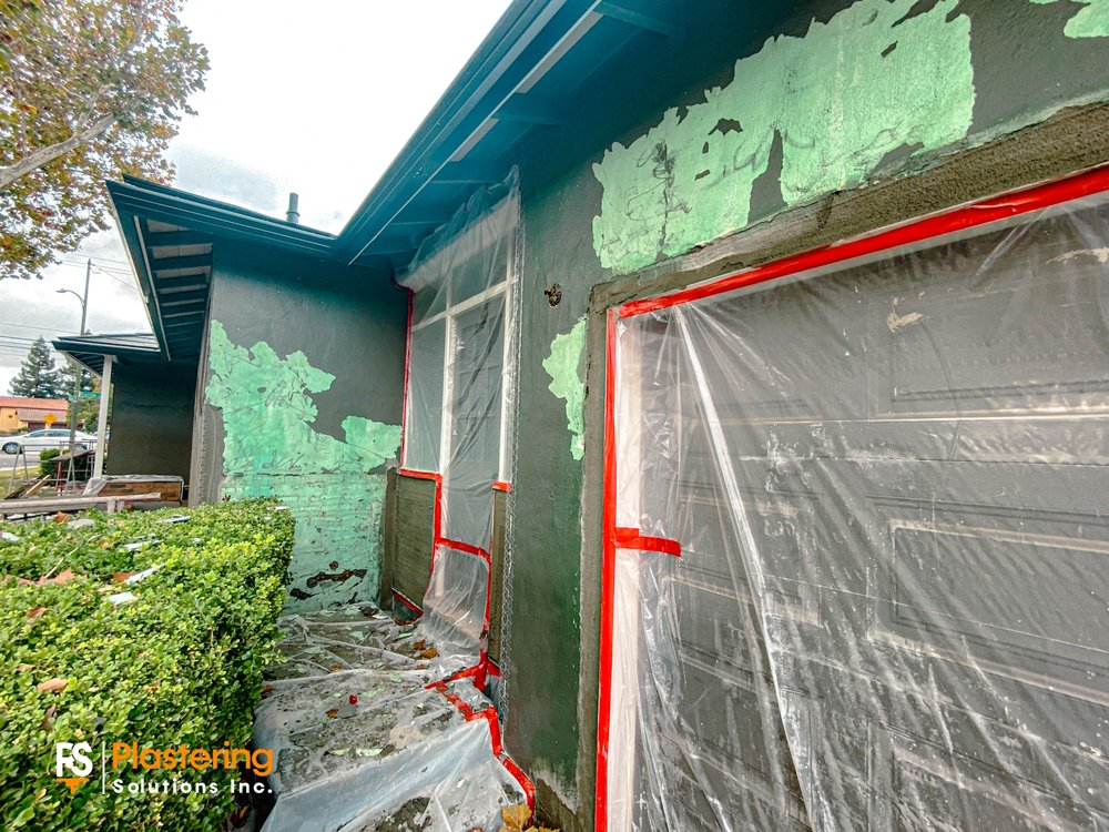 Old paint layers exposed around a masked garage door before new stucco