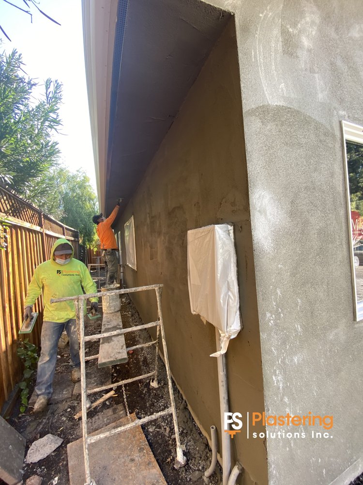 PSI crew applying stucco along a narrow side wall from scaffolding