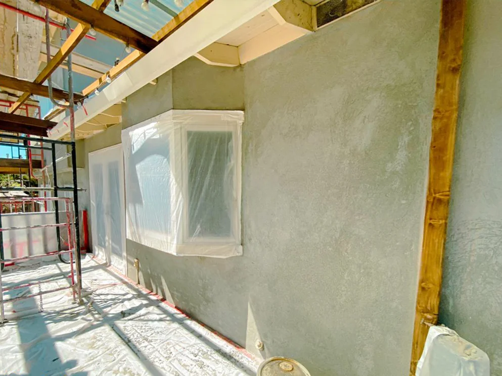 Close view of a resurfaced wall with a masked bay window before the finish coat