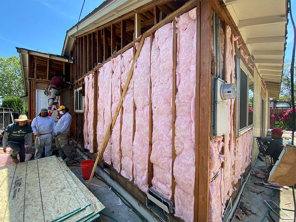 Crew working beside insulated wall framing after the siding came off