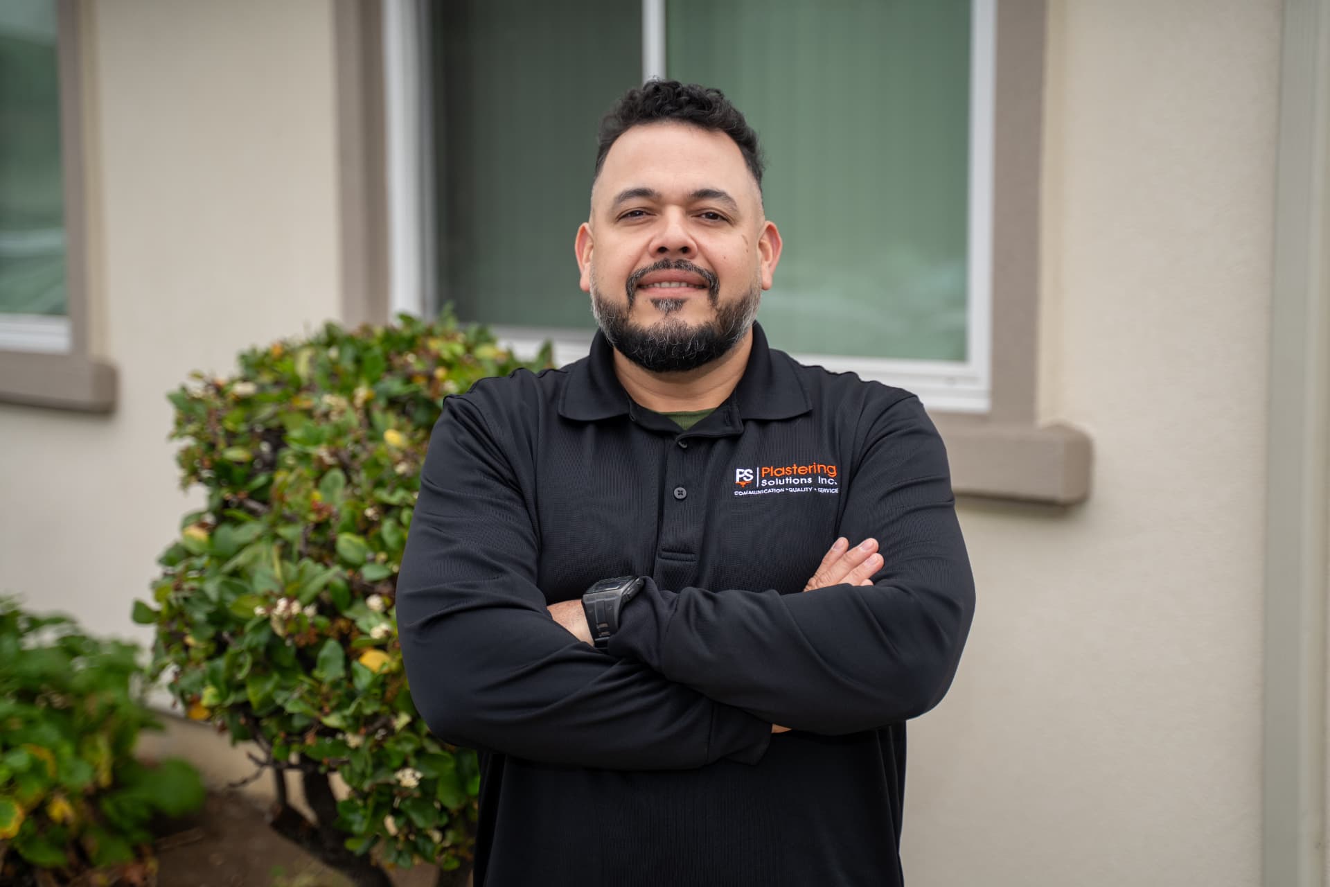 Jose Dominguez in a black Plastering Solutions Inc polo shirt, arms crossed, in front of a stucco home