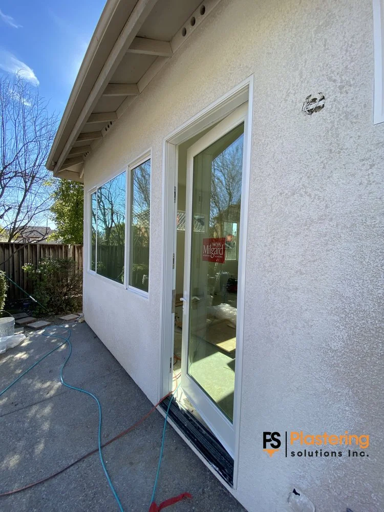 Completed replacement windows and glazed exterior door in a finished stucco wall