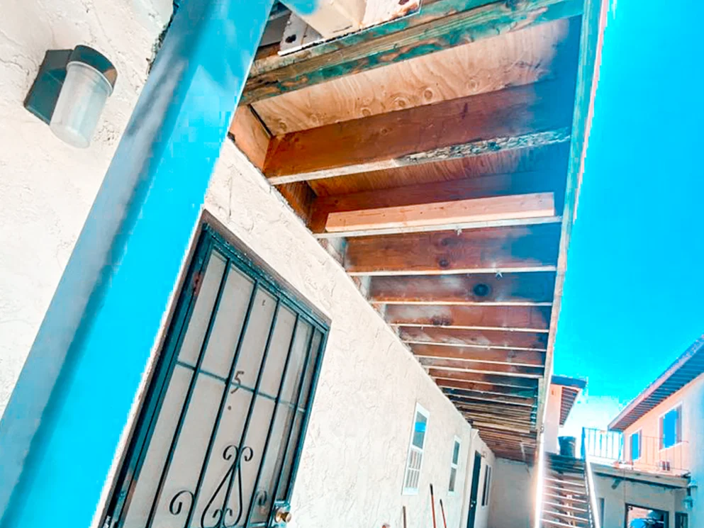 Rotted walkway framing opened above an apartment entry