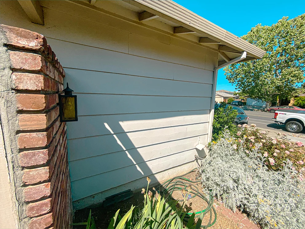Side wall with painted lap siding beside a brick column before conversion