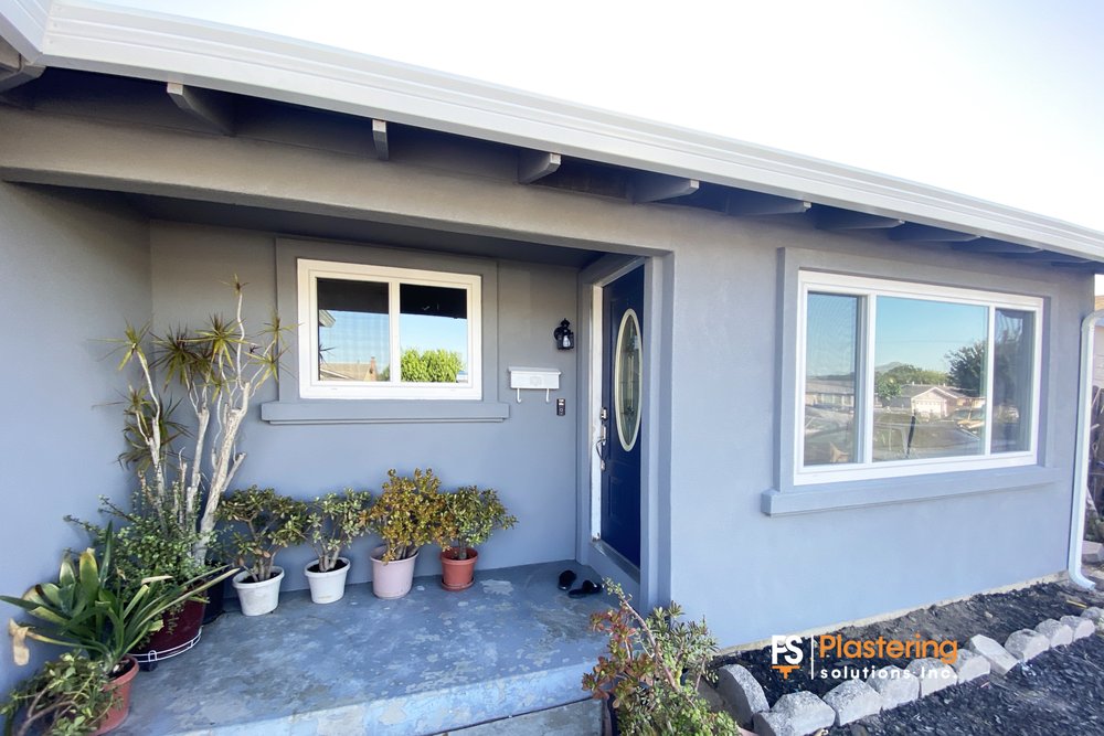 The same home after siding removal and a new stucco exterior in a grey finish