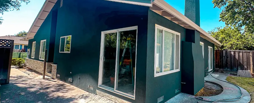 Single-story house with freshly painted dark green stucco walls, white window trim and sliding glass door
