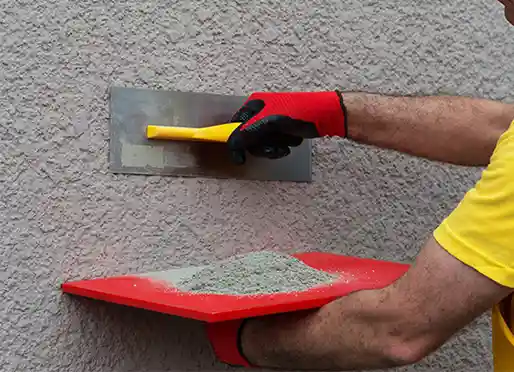 Plasterer in red gloves troweling stucco onto a wall from a hawk loaded with mix