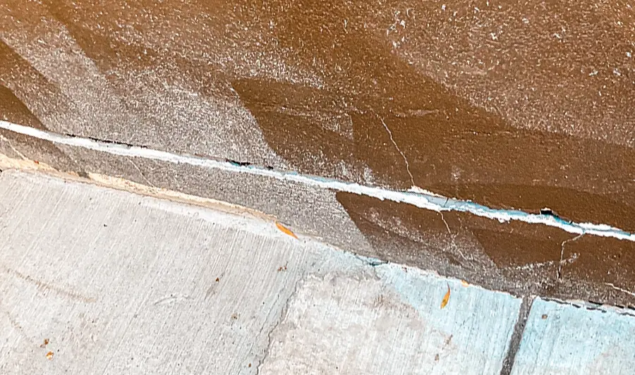 Long horizontal crack separating a brown stucco wall from the concrete slab at its base