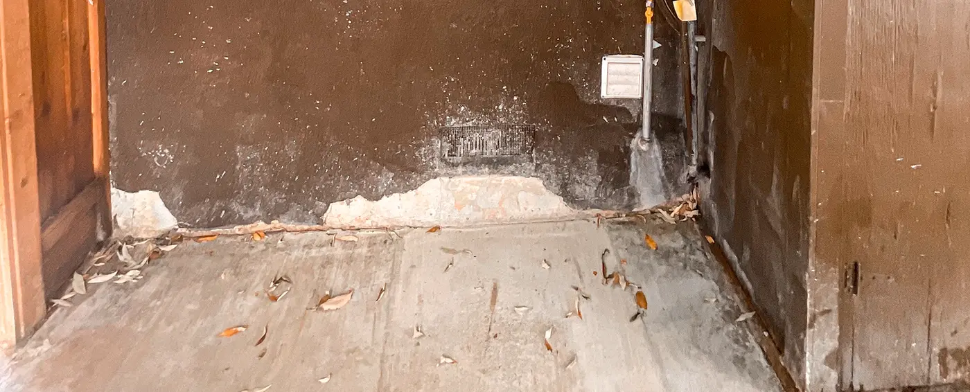 Water-stained stucco wall with crumbling plaster along its base where it meets a concrete floor