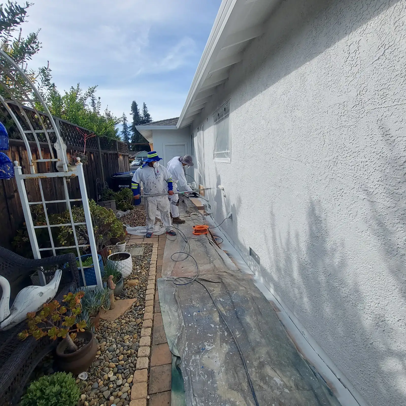 Plastering Solutions crew painting a residential exterior along a protected side yard