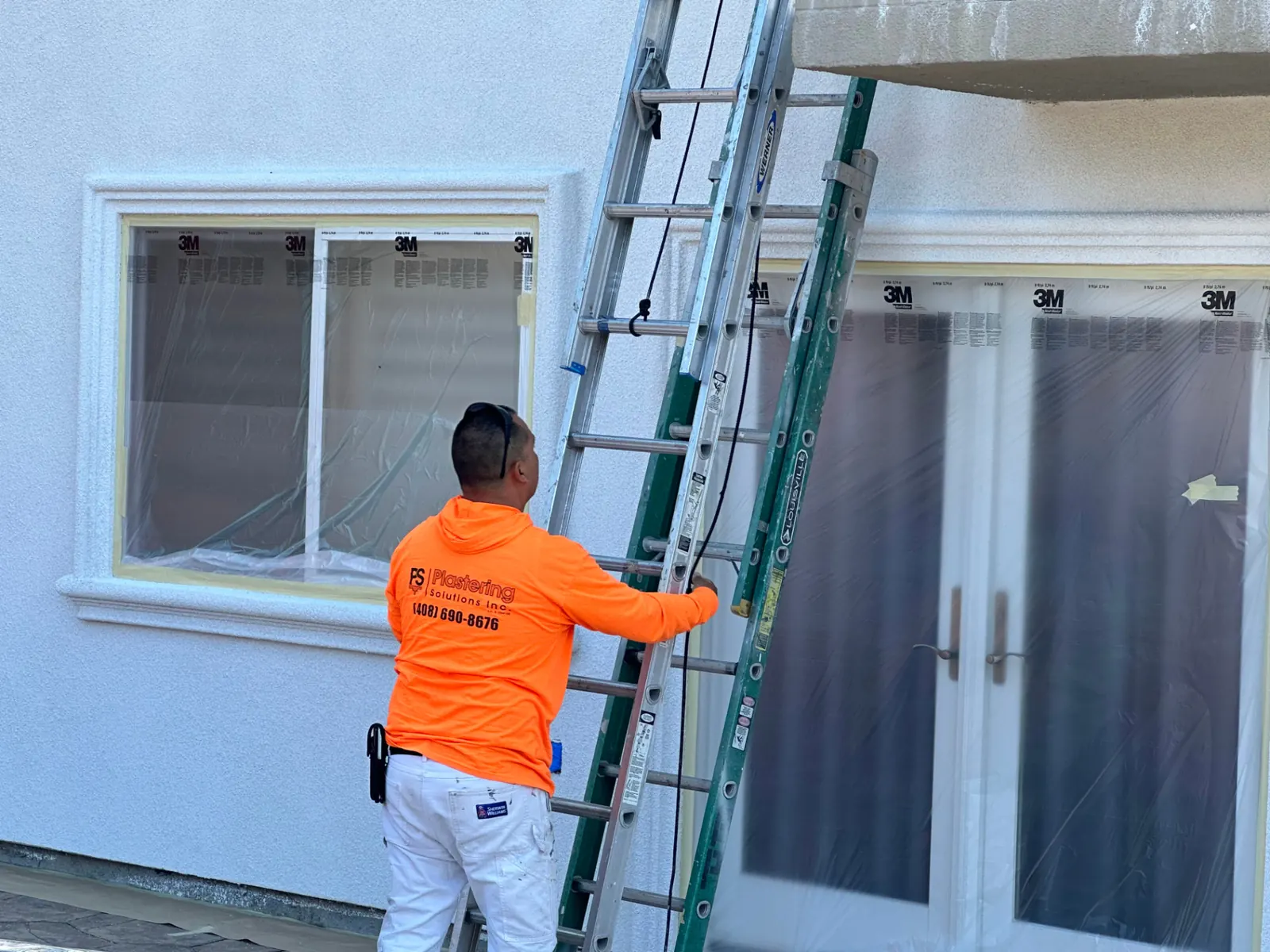 Plastering Solutions team member reviewing ladder access beside protected windows during a painting estimate