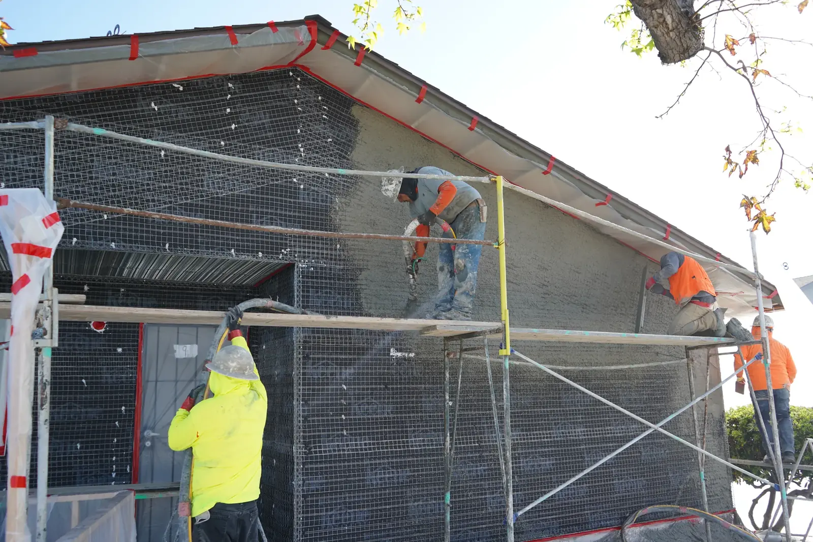 Plasterers applying the scratch coat from scaffolding while a crew member feeds the hose