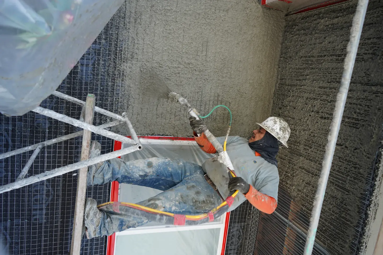 Plasterer spraying stucco inside a recessed apartment entry above a masked window