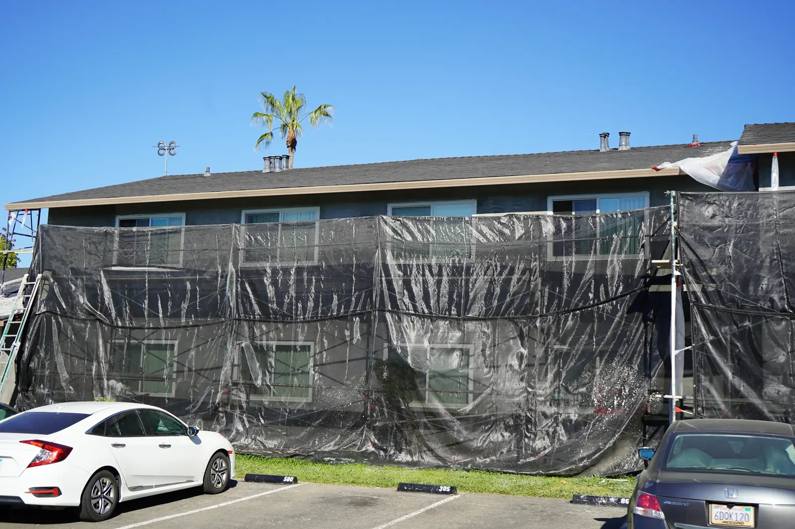 Two-story apartment building wrapped in protective scaffold netting beside the parking lot