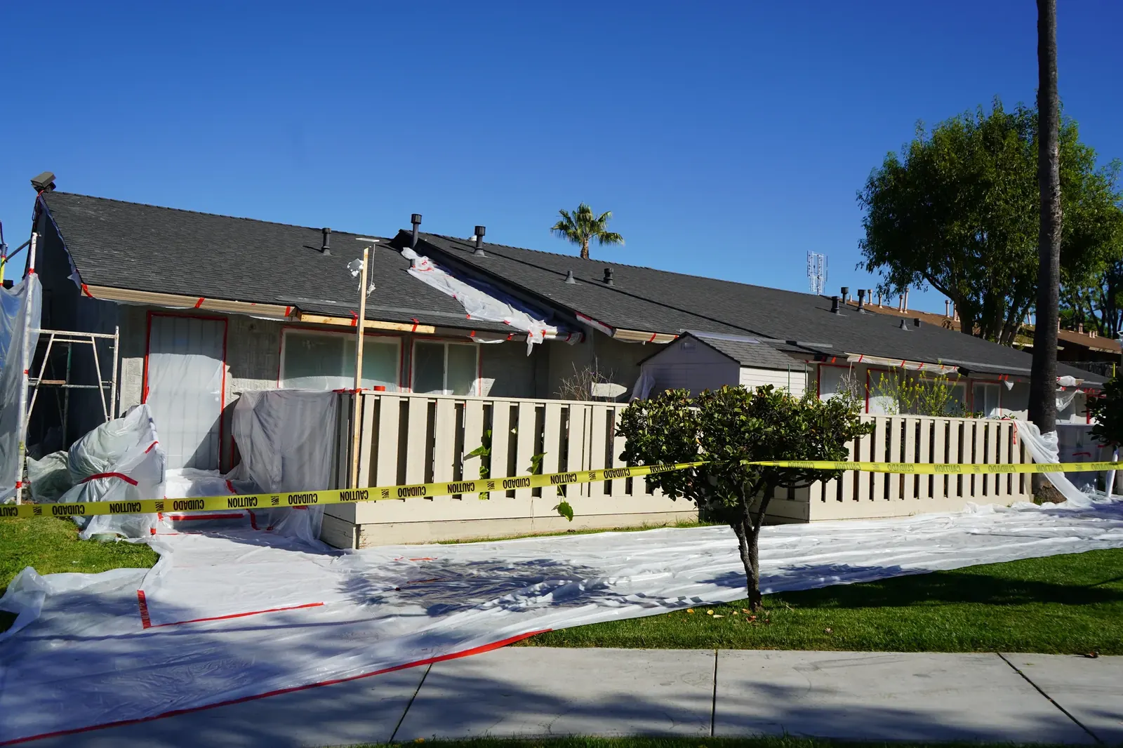 Rear apartment units with caution tape and protected lawn during stucco application