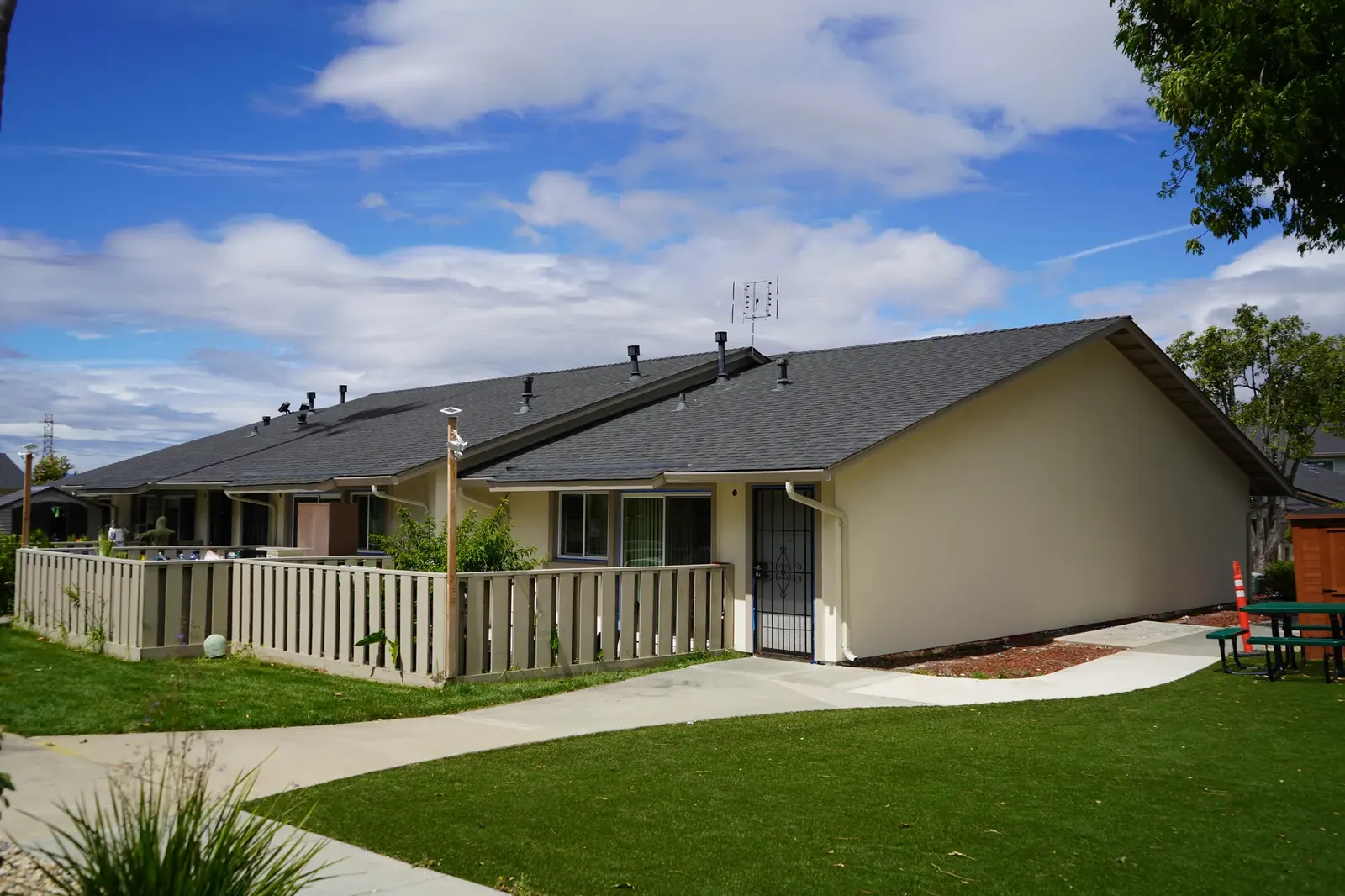 Completed single-story apartment units with cream stucco, fencing, and new walkway