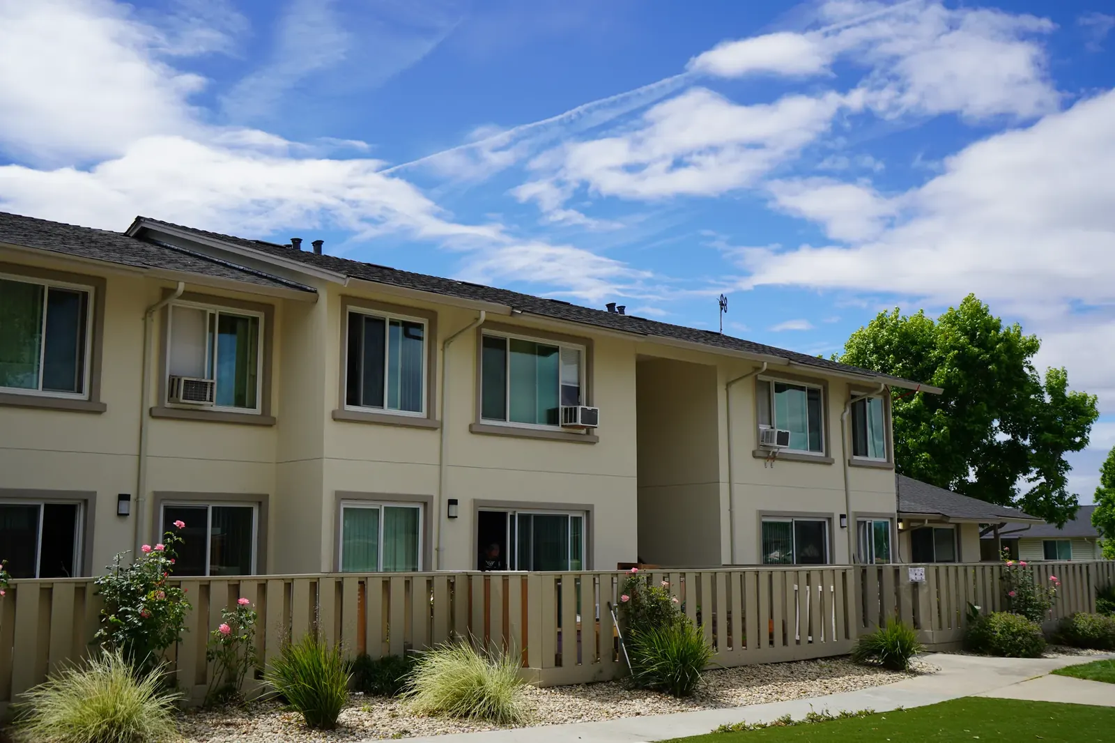 Finished two-story Mayfair apartments with cream stucco, window trim, and landscaping