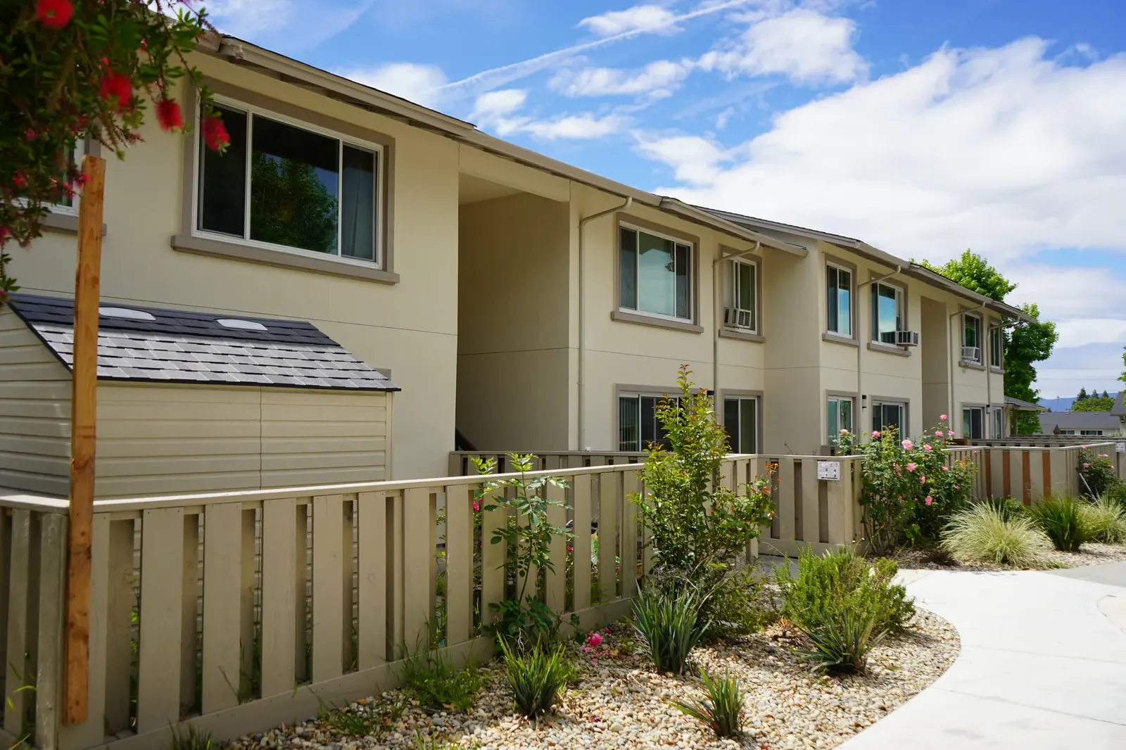 Completed apartment row with cream stucco, fenced patios, and a curved walkway