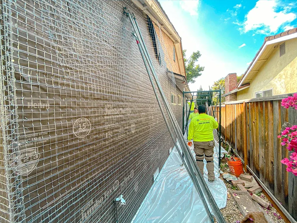 Crew member walking the side yard beside a wall wrapped in lath