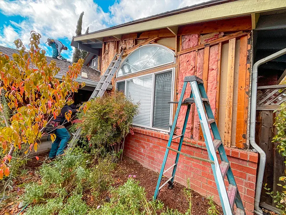 Siding removed around an arched window with the crew working on the roof