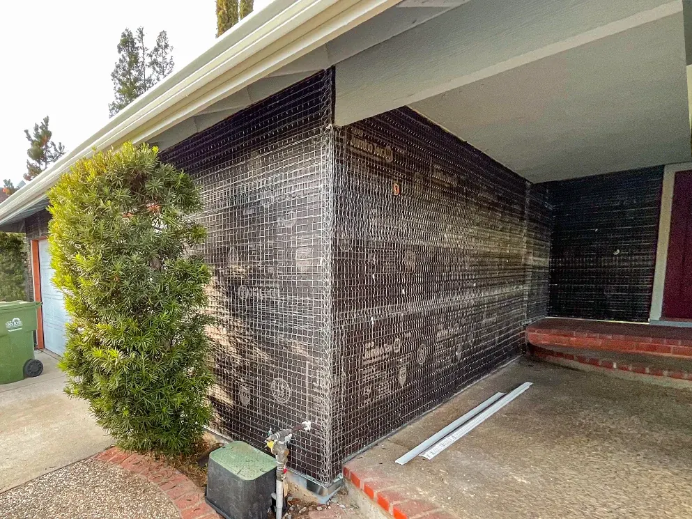 Front corner wrapped in building paper and lath beside the entry