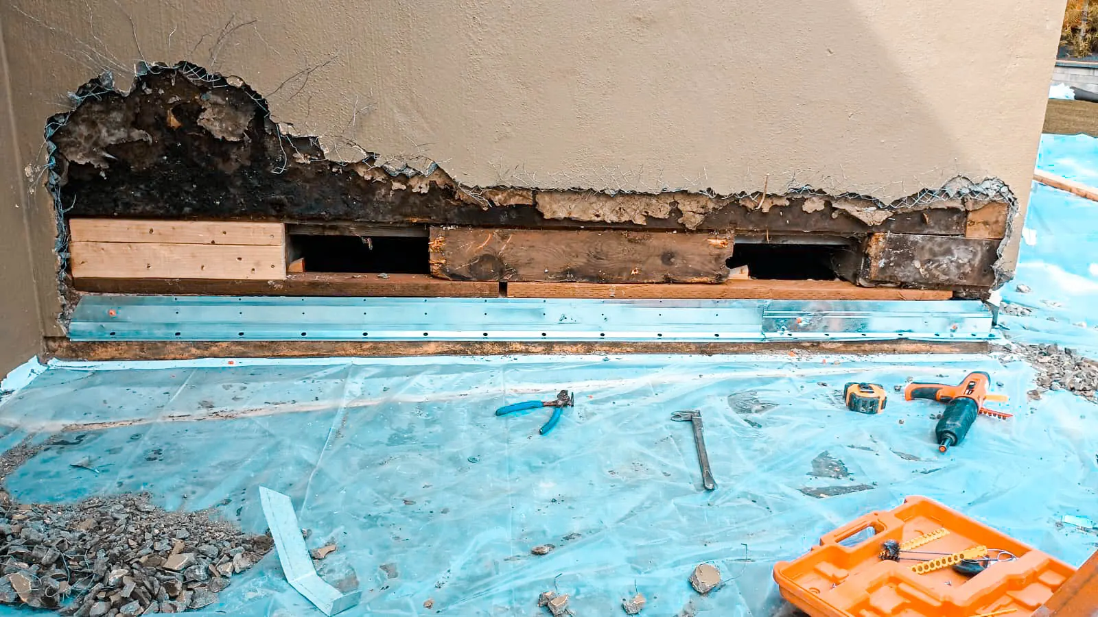 Stucco wall opened along its base to expose what sits behind the bottom of the assembly