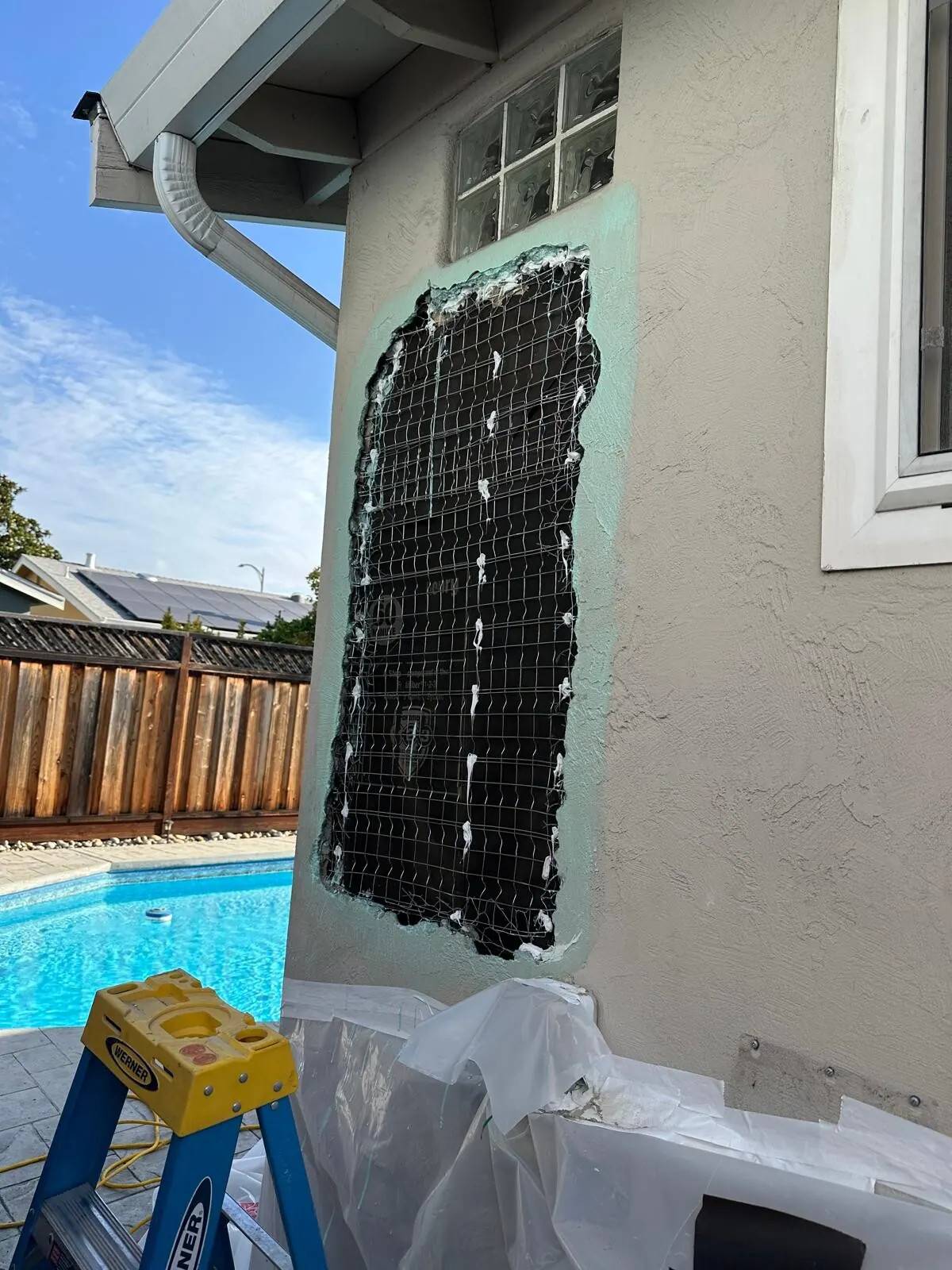 Stucco wall opened to expose metal lath during patch preparation beside a backyard pool