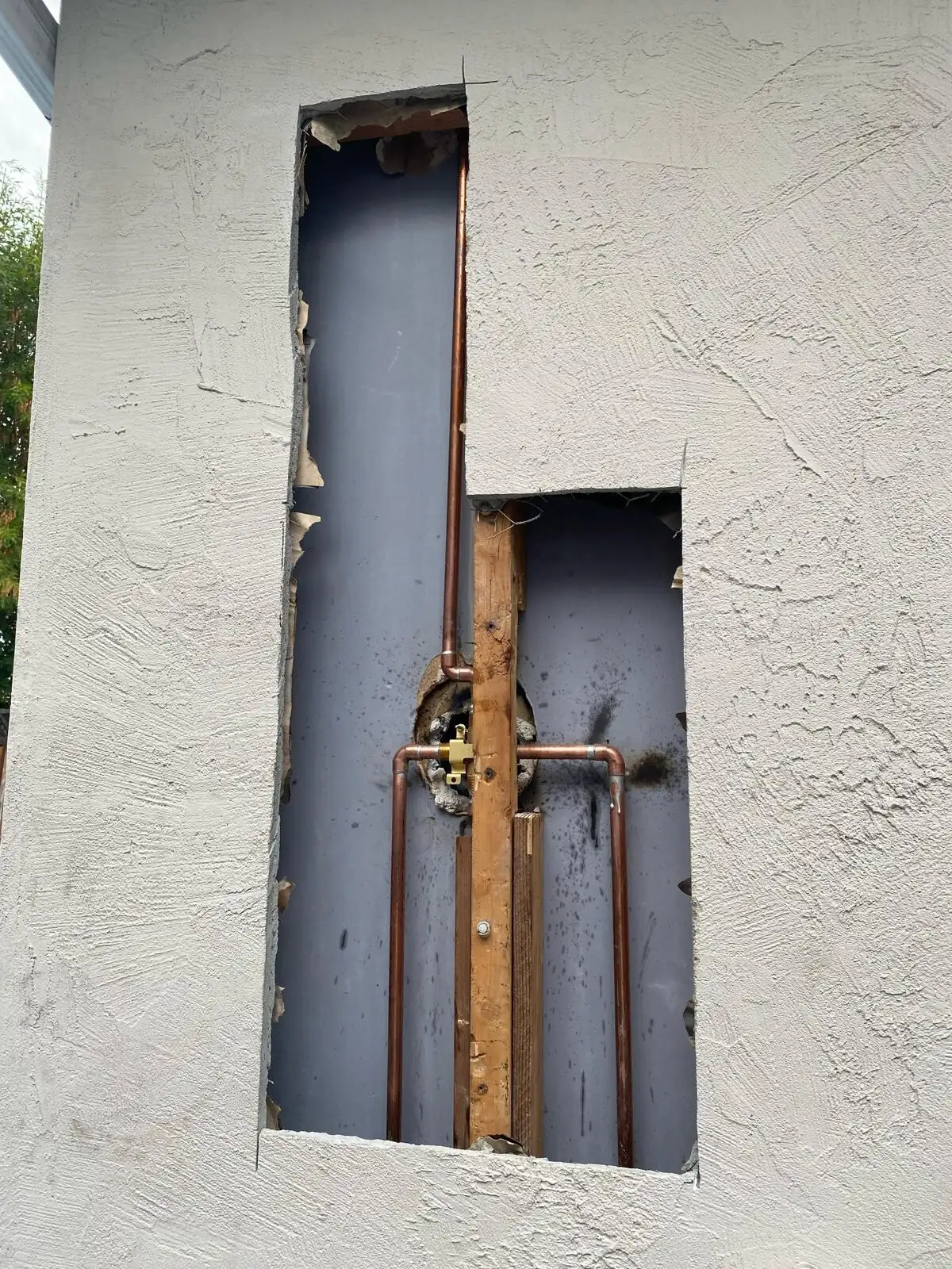 Exterior stucco opened to expose wall framing, building paper and copper plumbing during repair work