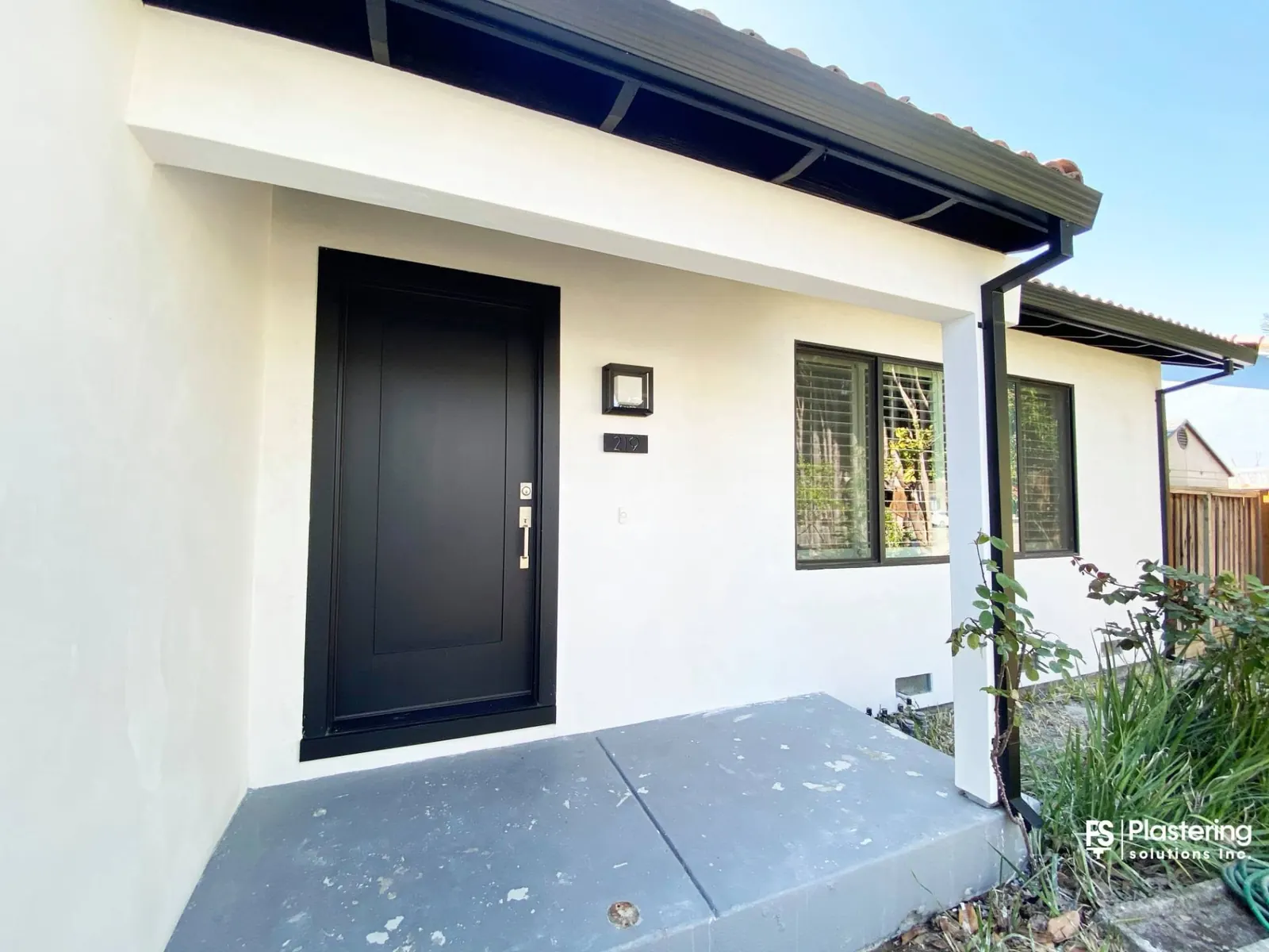 Front entry of a home finished in smooth white stucco with a black door